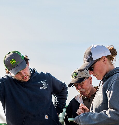 Father and his adult children standing next to the tail gate of a pickup truck looking the daughter's mobile device in Alberta, Canada